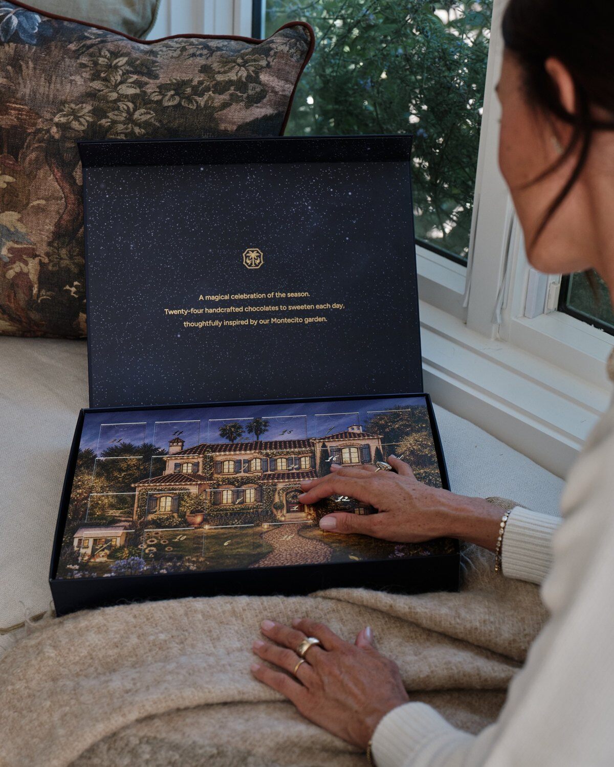 A woman opening the As Ever Holiday Advent Calendar, with an illustration of a Montecito house inside the lid