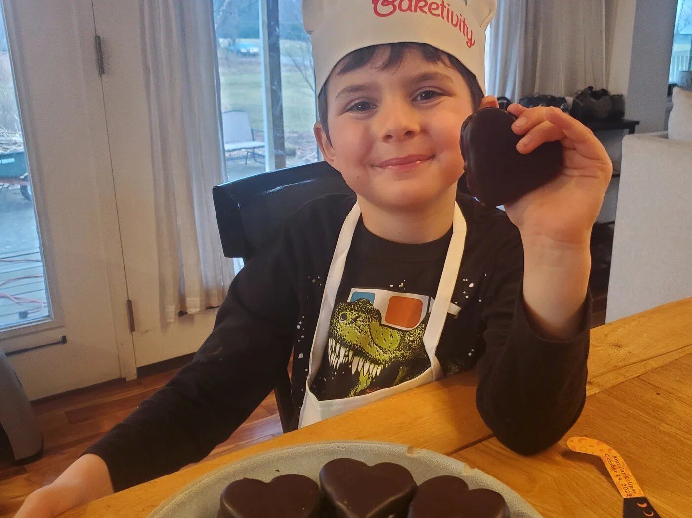 Smiling boy in a Baketivity chef hat holding a heart shaped treat