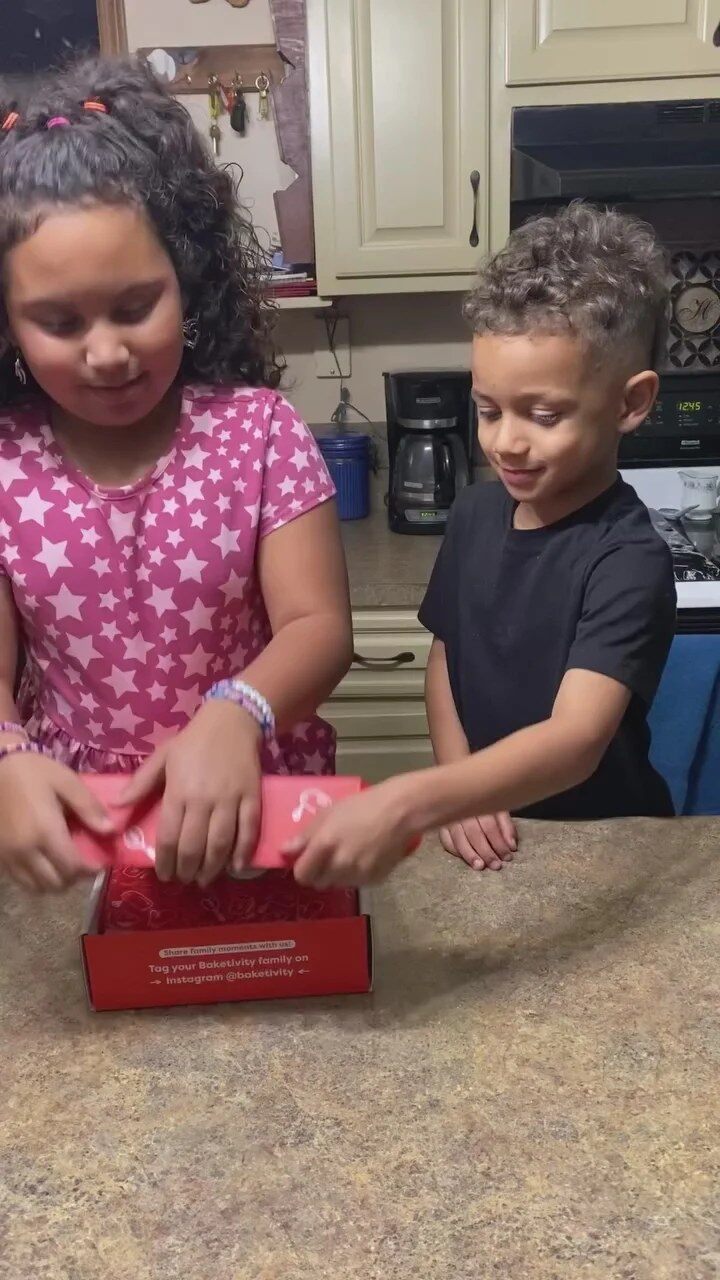 Two kids opening a Baketivity baking kit on the kitchen counter