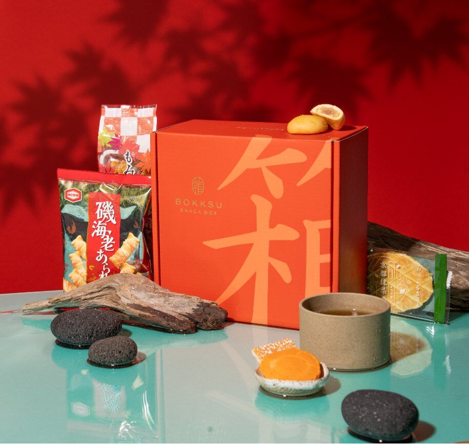 The Bokksu October 2026 Koyo Downstream box with Japanese autumn snacks and tea against red maple leaves