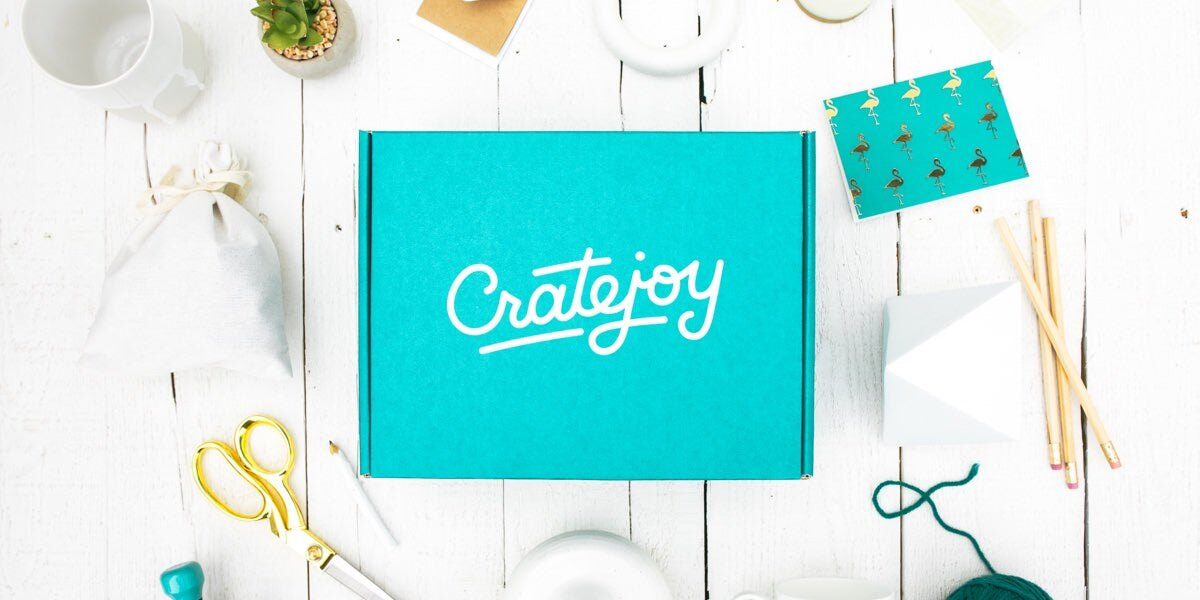 A teal Cratejoy box on a white table surrounded by stationery, yarn and craft supplies