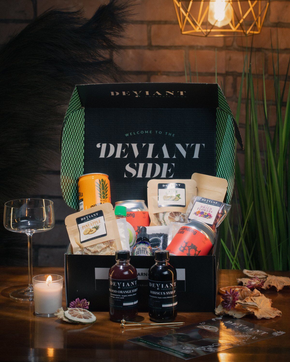 An open Deviant Cocktail Club box with syrups, garnishes and cocktail ingredients on a bar counter