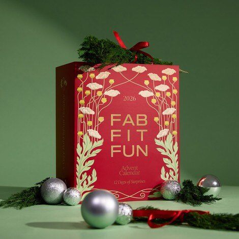 The FabFitFun 2026 Holiday Advent Calendar, a red and gold floral box topped with greenery and a red ribbon, next to silver ornaments