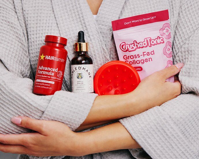 A woman in a robe holding IPSY Wellness supplements, a serum bottle and a collagen pouch