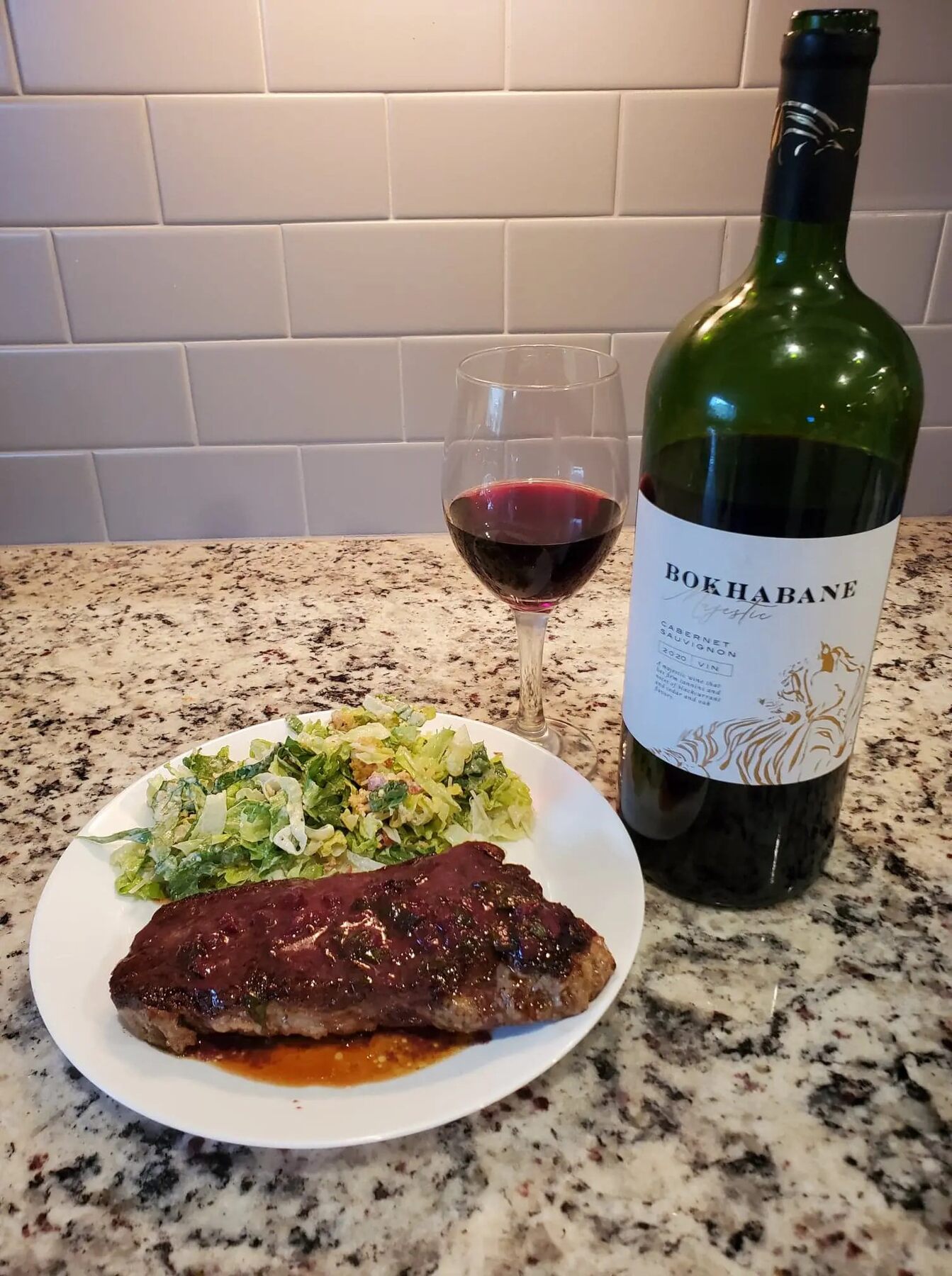 Bottle of Bokhabane red wine with a glass and a steak dinner