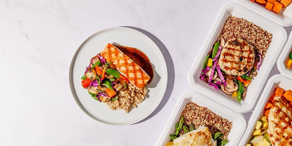 Trifecta prepared meals in containers next to a plated salmon dish